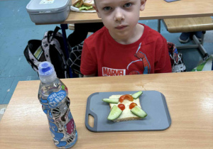 Uśmiechnięty chłopiec siedzi przy stoliku a przed nim kolorowa kanapka