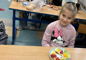 Uśmiechnięta dziewczynka siedzi przy stoliku a przed nią kolorowa kanapka