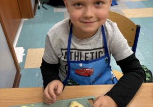 Uśmiechnięty chłopiec siedzi przy stoliku a przed nim kolorowa kanapka