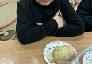 Uśmiechnięty chłopiec siedzi przy stoliku a przed nim kolorowa kanapka