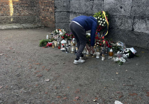 Chłopak stawia znicz pod ścianą