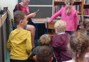 Radosne dzieci siedzą w bibliotece z kobietą