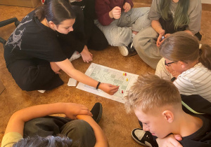 Uczniowie siedzą przy stoliku i grają na podłodze w gry planszowe