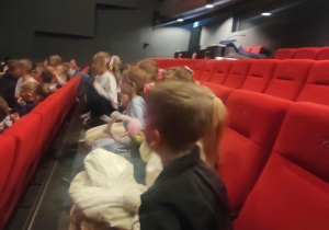 Radosne dzieci siedzą na fotelach w teatrze.
