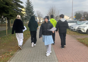 Uczniowie idą chodnikiem, w rękach trzymają ulotki