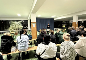 Kobieta w stroju policyjnym stoi przed grupą ludzi