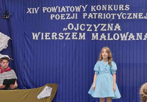 Dziewczynka w niebieskiej sukience stoi na scenie