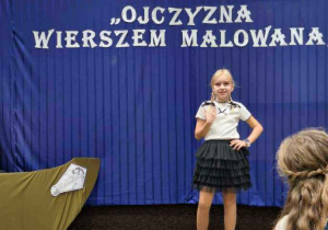 Dziewczynka w stroju galowym stoi na scenie