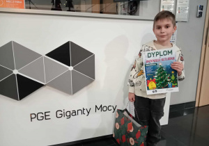 Uśmiechnięty chłopiec z torbą i dyplomem w dłoniach