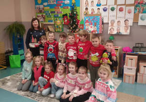 Radosne dzieci z panią ubrane w świąteczne swetry