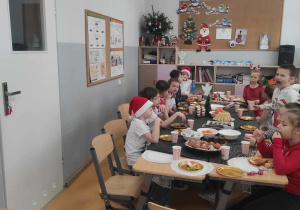 Uśmiechnięte dzieci siedzą przy stole wigilijnym w klasie 2c