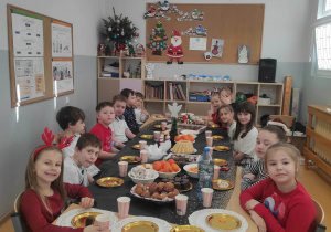 Uśmiechnięte dzieci siedzą przy stole wigilijnym w klasie 2c