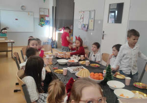Uśmiechnięte dzieci siedzą przy stole wigilijnym w klasie 2c