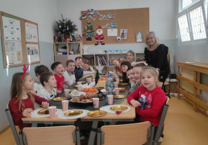 Uśmiechnięte dzieci siedzą przy stole wigilijnym w klasie 2c