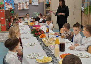 Dzieci siedzą przy stole, obok stoi kobieta