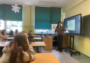 Dziewczynki siedzą w ławkach, a prelegentka omawia układ rozrodczy kobiety