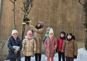 Pani wiesza na drzewie karmę dla ptaków