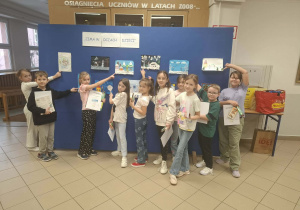 Uśmiechnięte dzieci na tle granatowej tablicy z rysunkami o tematyce zimowej