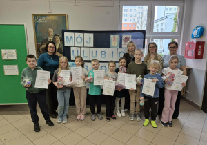 Grupa uśmiechniętych dzieci z nagrodami, z tyłu kobiety