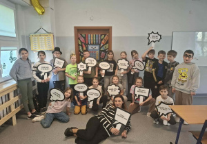 Dzieci z radosnymi uśmiechami pokazują tabliczki z napisami