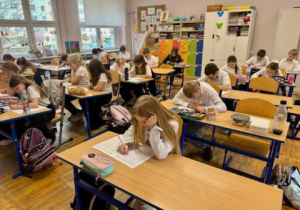 Dzieci siedzą w ławkach i rozwiązują test