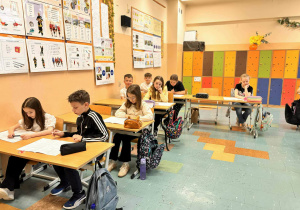 Dzieci siedzą w ławkach i rozwiązują test