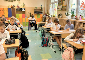 Dzieci siedzą w ławkach i rozwiązują test