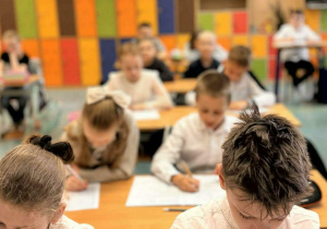 Dzieci siedzą w ławkach i rozwiązują test