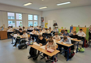 Dzieci siedzą w ławkach i rozwiązują test