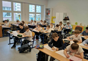 Dzieci siedzą w ławkach i rozwiązują test