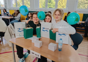 Uśmiechnięci uczniowie z prezentami siedzą przy stoliku