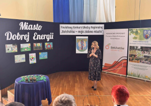 Kobieta mówi do mikrofonu, za nią dekoracja z napisem Miasto dobrej energii