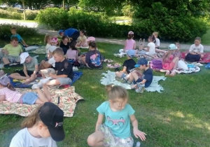 Radosne dzieci czytają książki siedząc na kocach na trawie.