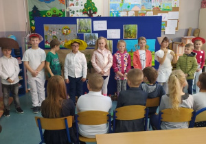 Dzieci na spotkaniu z panią leśnik mówią wiersz w grzybowych czapkach na głowie